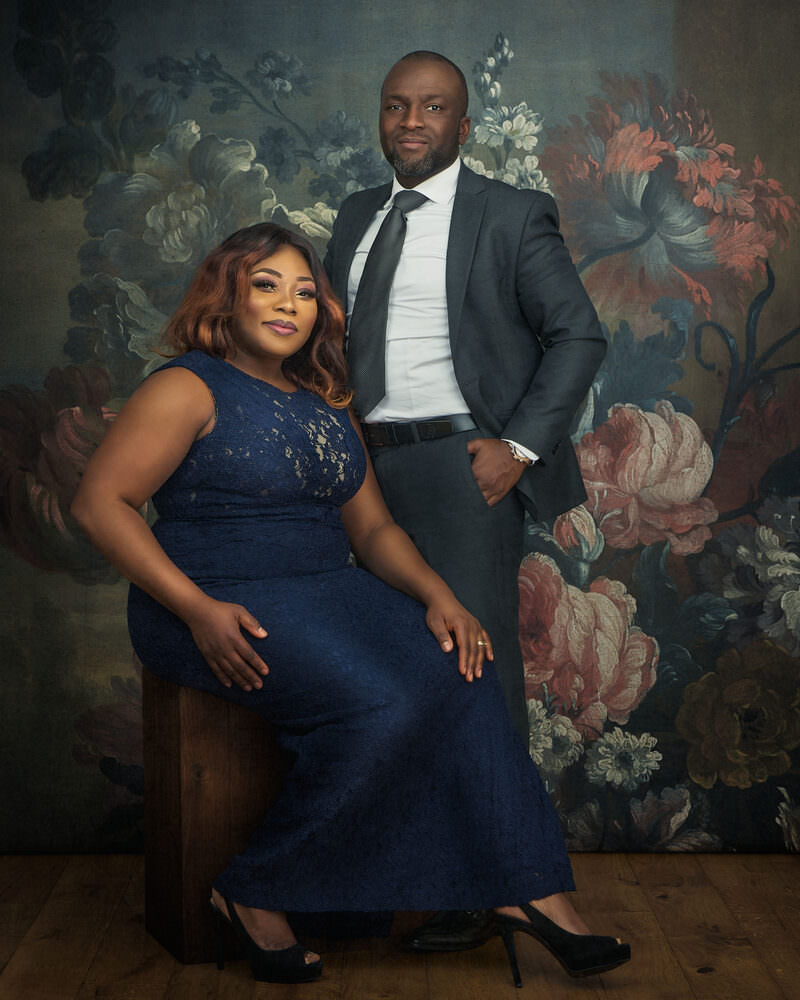 Elegant couple in formal attire posed against a painterly floral backdrop