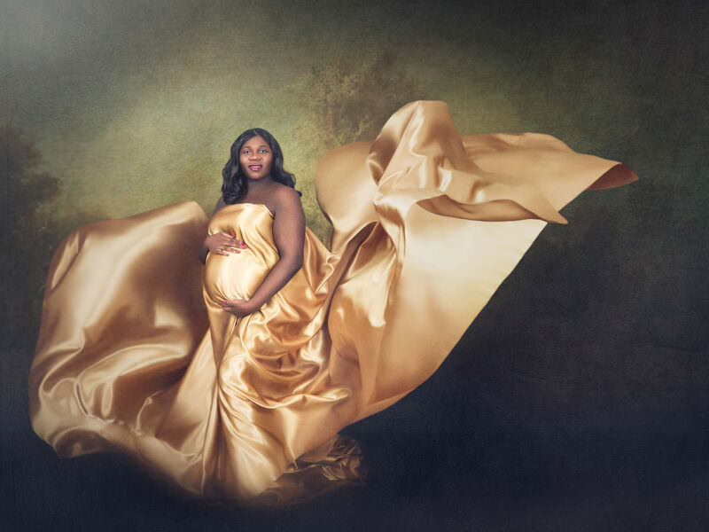 Painterly fine art maternity portrait of an expectant mother draped in flowing gold silk against an Old Masters backdrop