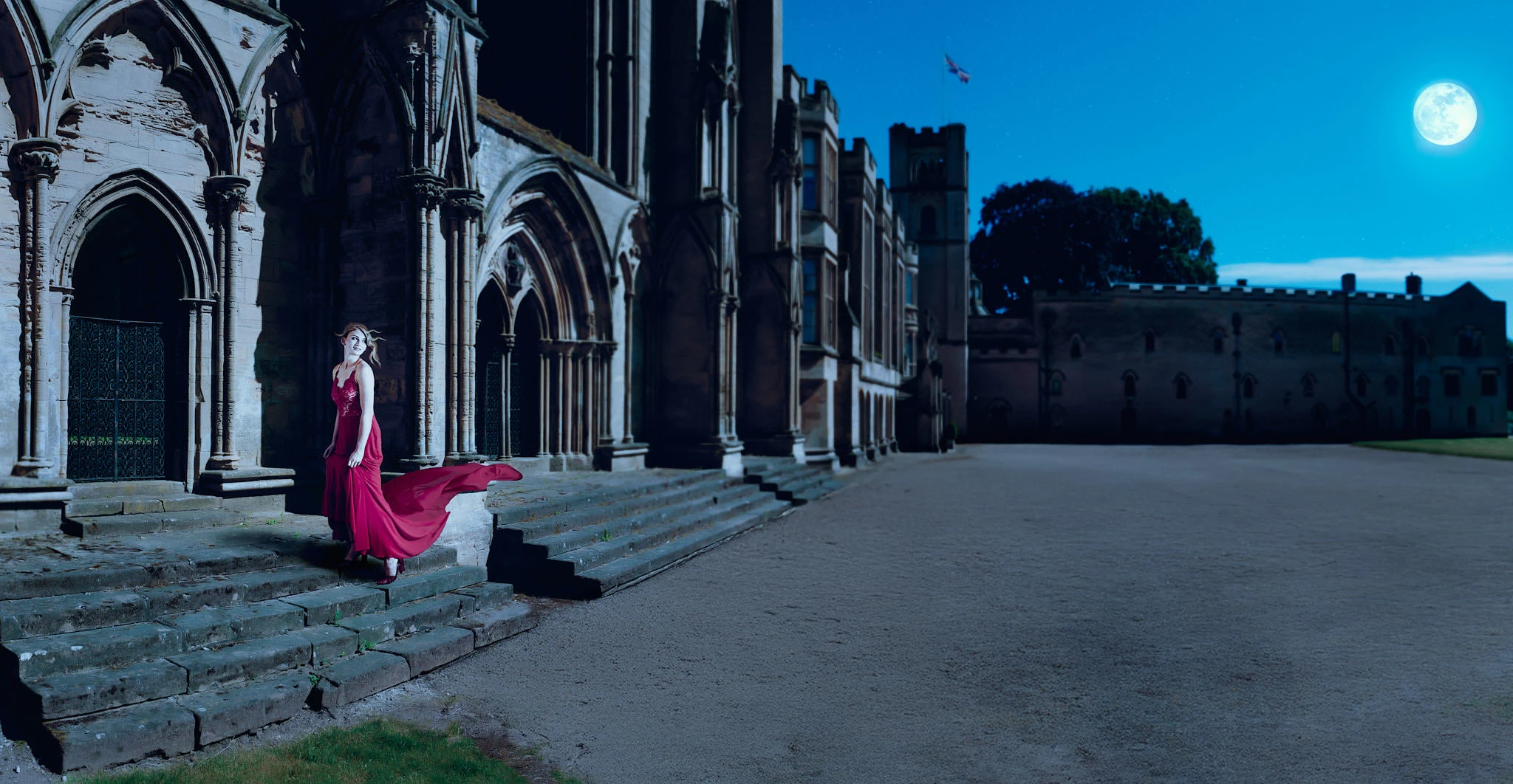 Dramatic portrait of a woman in a flowing red gown on castle steps under moonlight
